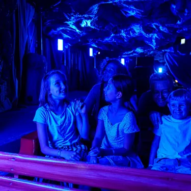 Eine fünfköpfige Familie sitzt im Boot der Drachengrotte im Heide Park Resort. Sie sind in der dunklen Höhle und schauen sich gespannt um.