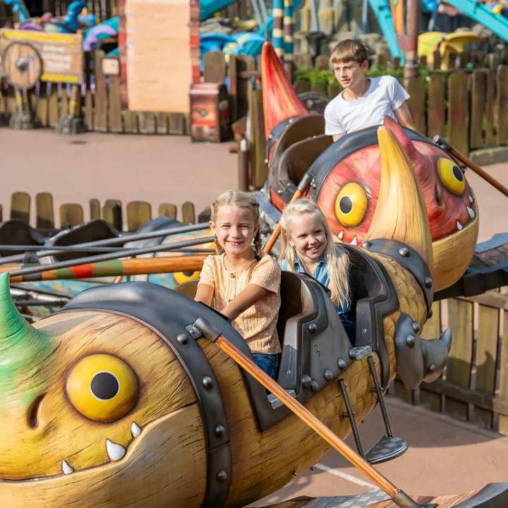 Zwei fröhliche Mädchen sitzen in der Gondel von Grobians Wolkenspringer im Heide Park Resort. Die Gondeln sind bunte Drachen.