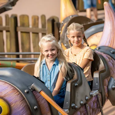Zwei fröhliche Mädchen sitzen in der Gondel von Grobians Wolkenspringer im Heide Park Resort. Die Gondeln sind bunte Drachen.