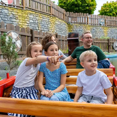 Eine Familie mit drei Kindern sitzen im Wikingerboot und erkunden die Attraktion "Drachengrotte" im Heide Park Resort.