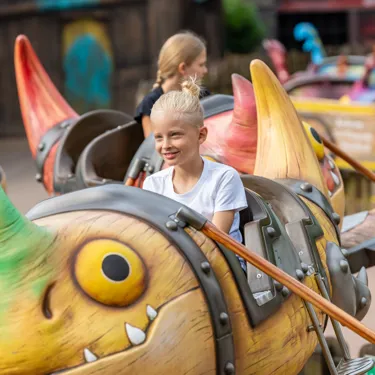 Ein fröhlicher Junge sitzt in der Gondel von Grobians Wolkenspringer im Heide Park Resort. Die Gondeln sind bunte Drachen.