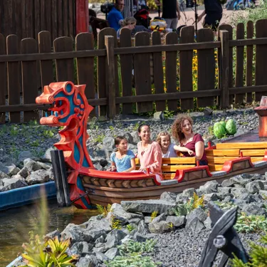 Zwei Frauen und zwei Mädchen sitzen im Wikingerboot und fahren durch eine steinige Landschaft im Heide Park Resort
