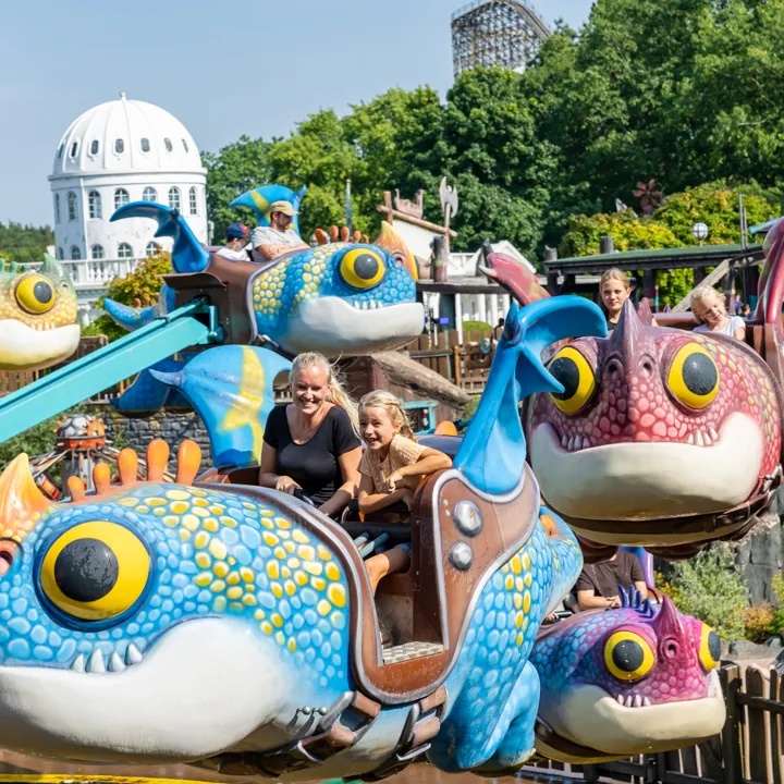 Kinder fahren fröhlich mit einem größen Drachen im Themenbereich „Drachenzähmen – Die Insel“ im Heide Park Resort.