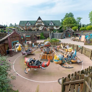 Besucher sitzen in den Gondeln von Grobians Wolkenspringer im Heide Park Resort. Die Gondeln sind bunte Drachen. Im Hintergrund sind weitere Drachenelemente.