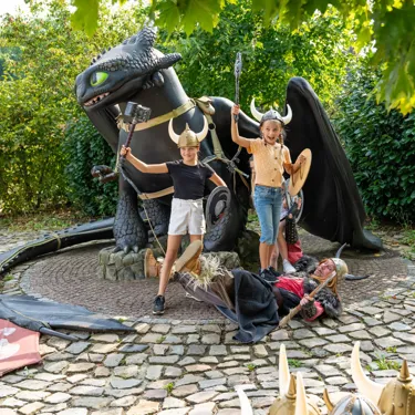 Zwei Mädchen spielen mit einem Wikinger bei einer großen Ohnezahn-Figur.