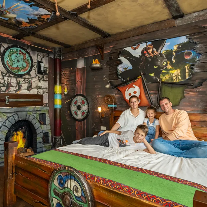 Eine vierköpfige Familie ist auf dem Bett im Drachenzimmer. Die Thematisierung ist von Drachenzähmen leicht gemacht mit Drachen- und Wikinger-Elementen.