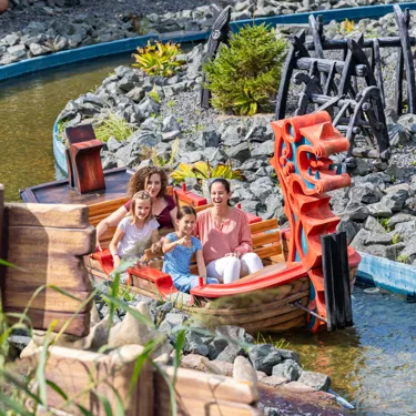 Zwei Frauen und zwei Mädchen sitzen im Wikingerboot und erkunden die Attraktion "Drachengrotte" im Heide Park Resort.